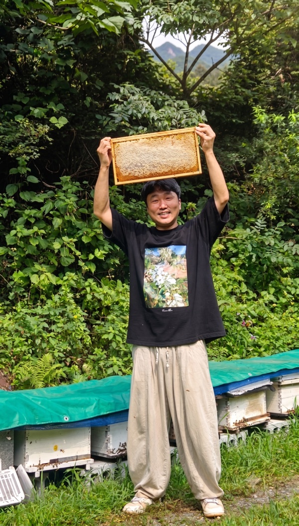 Hyunseok Seo holding a capped honey frame above his head at his apiary